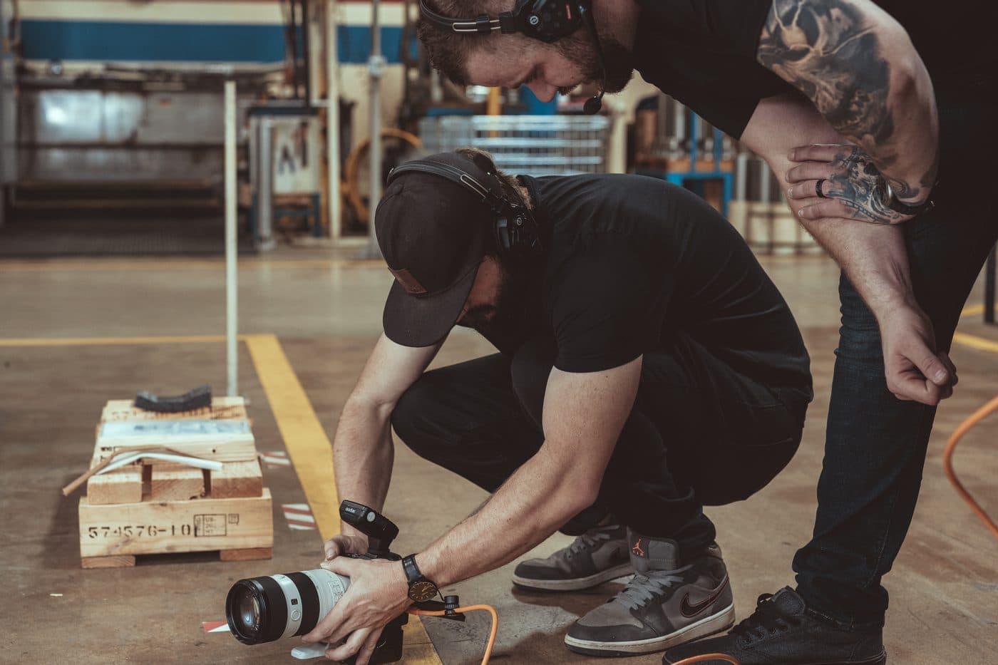 Two Hyped Visuals crew members in headphones set up a low-angle camera shot on a warehouse floor