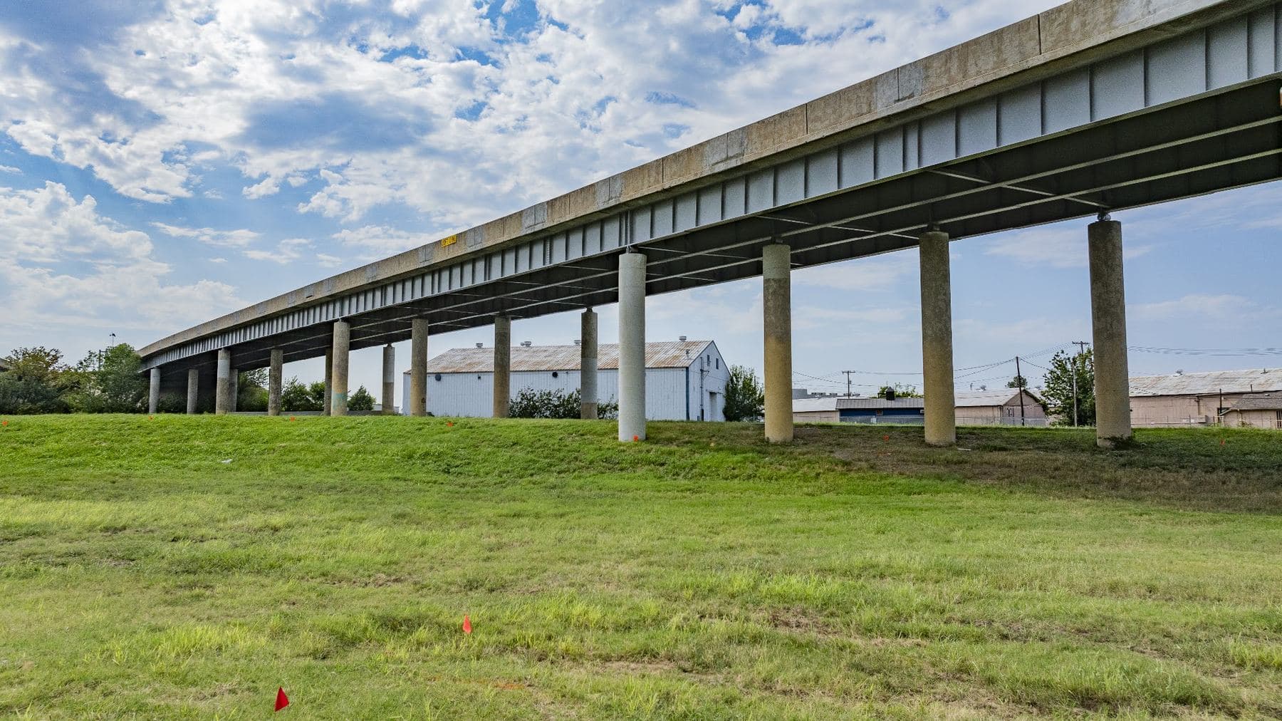 Ground level view of a long elevated highway carried on concrete columns under a partly cloudy sky