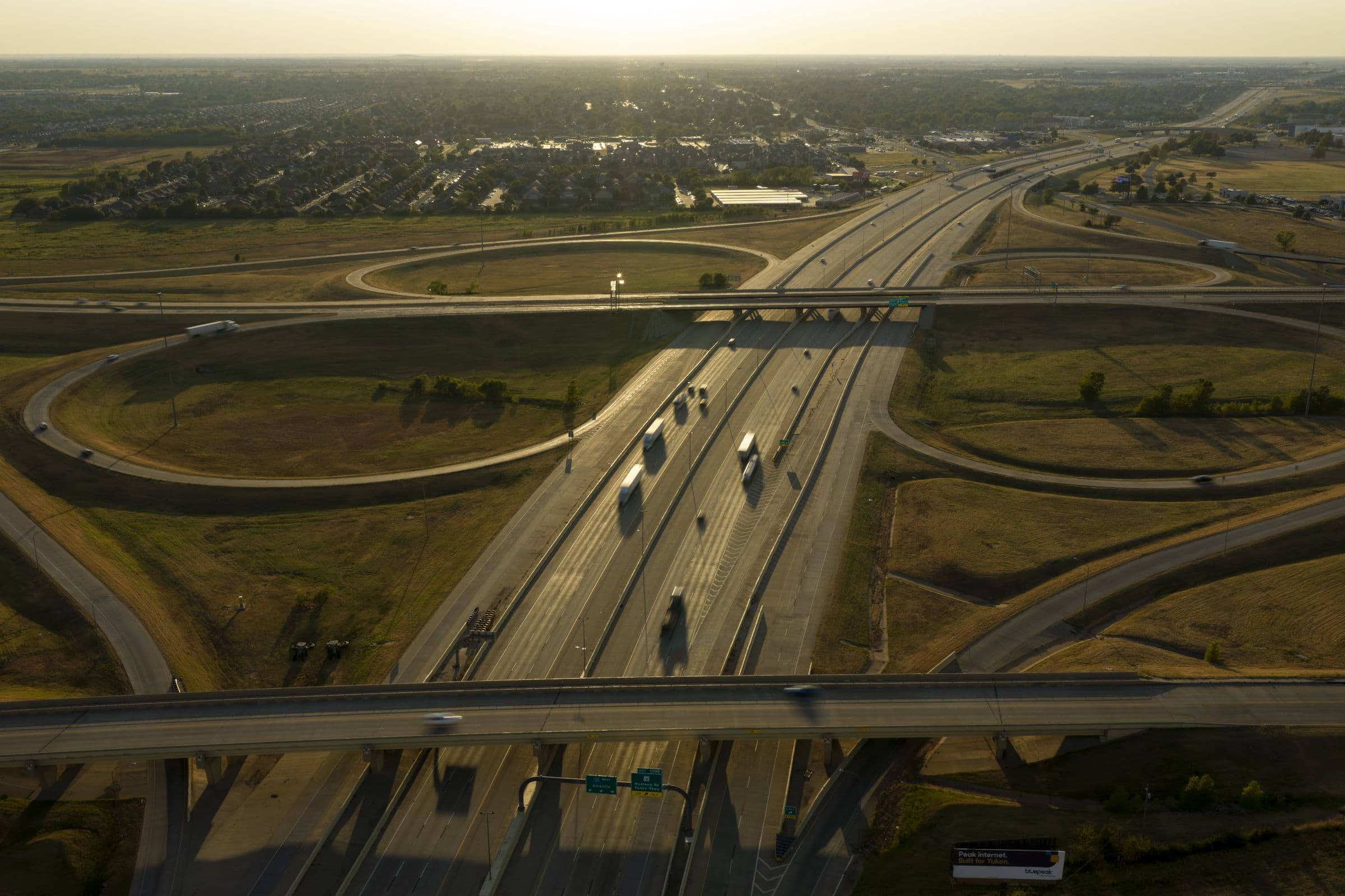Aerial view at golden hour of a cloverleaf highway interchange, with truck traffic moving through the center lanes