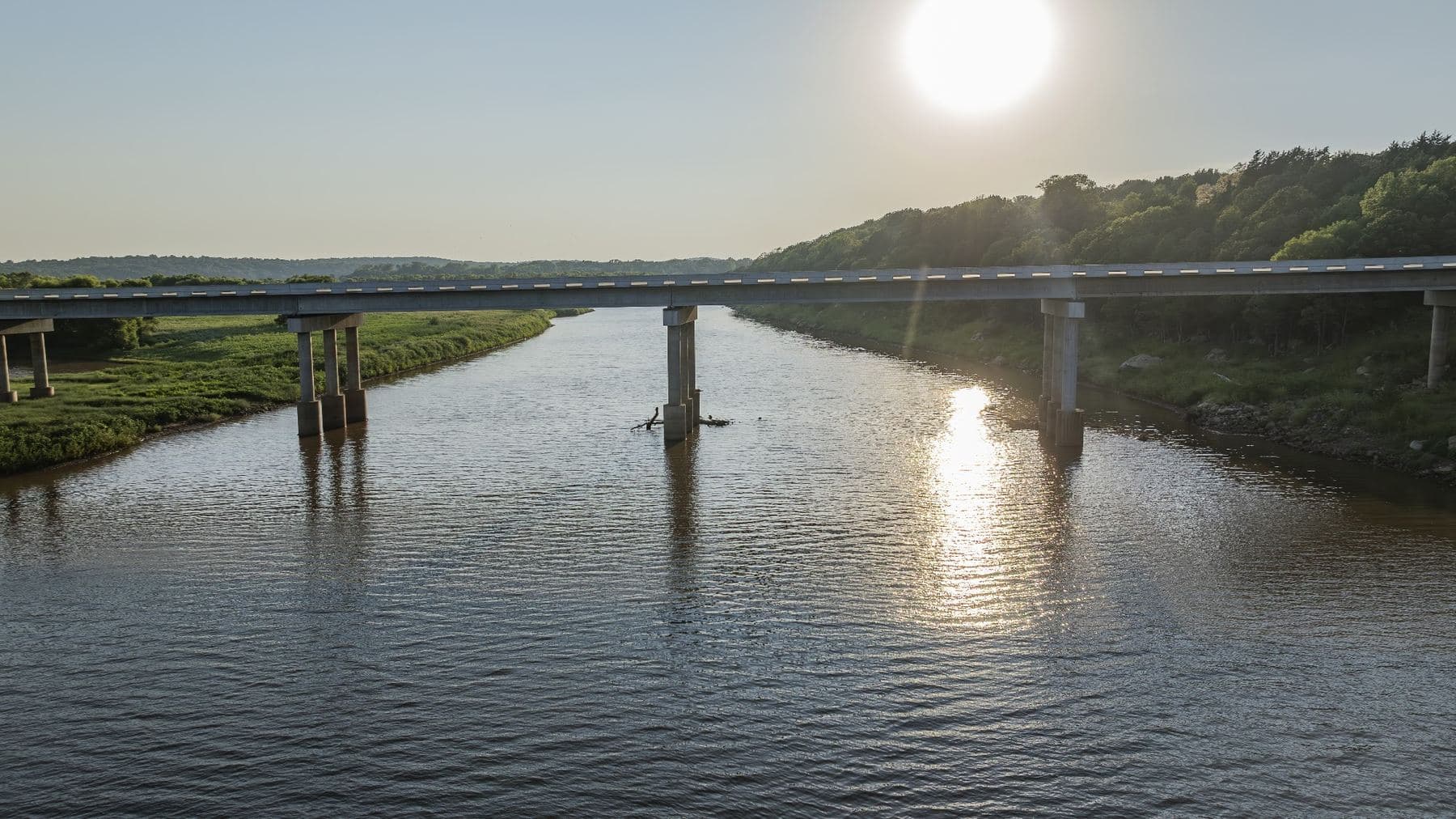 Low sun over a multi span highway bridge crossing a wide river, light reflecting off the water
