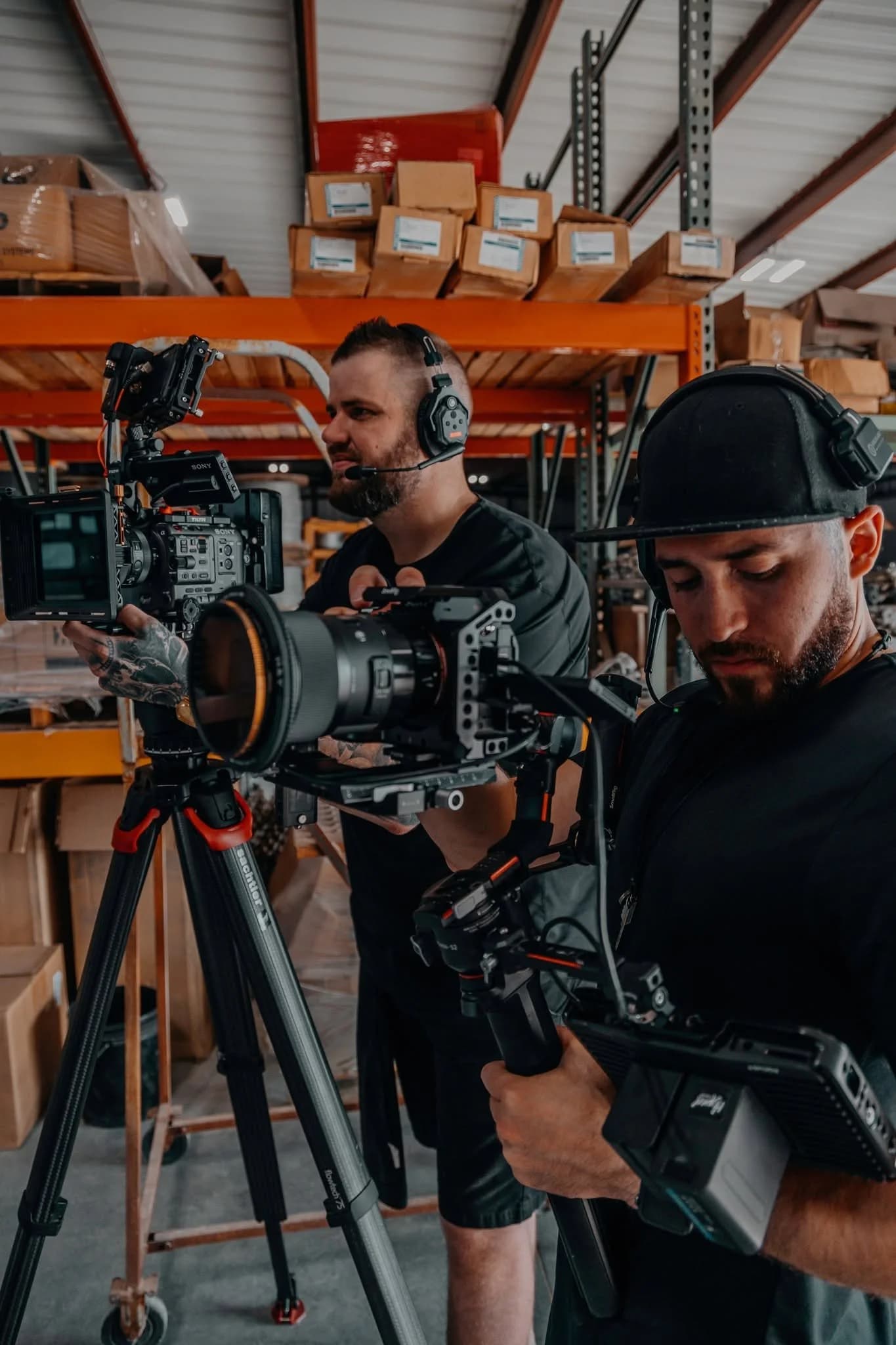 Two Hyped Visuals crew members in headphones working a cinema camera rig among warehouse shelving