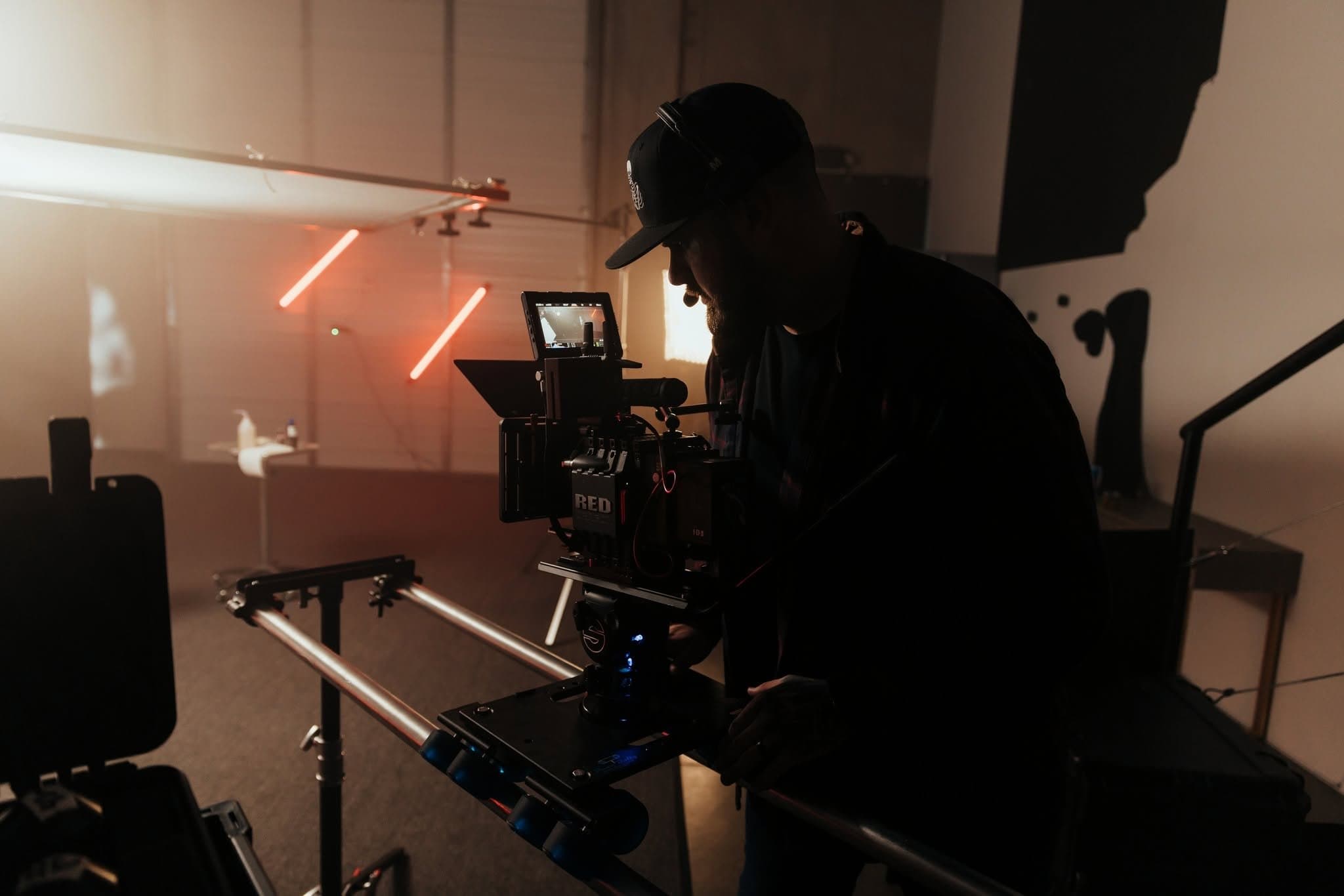 A Hyped Visuals camera operator, in silhouette, works a RED cinema camera on a slider on a set lit with red light tubes